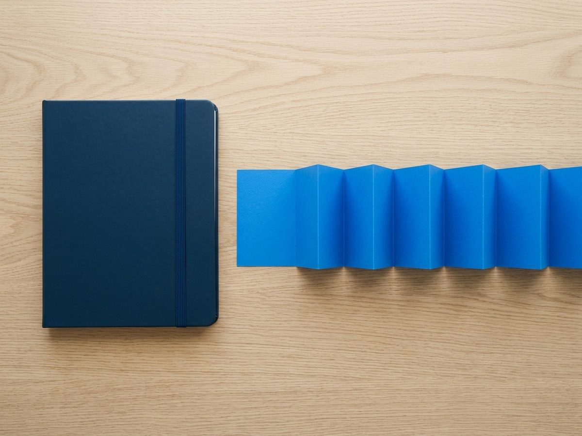 A closed navy notebook beside an unfolded blue accordion file on a wooden desk